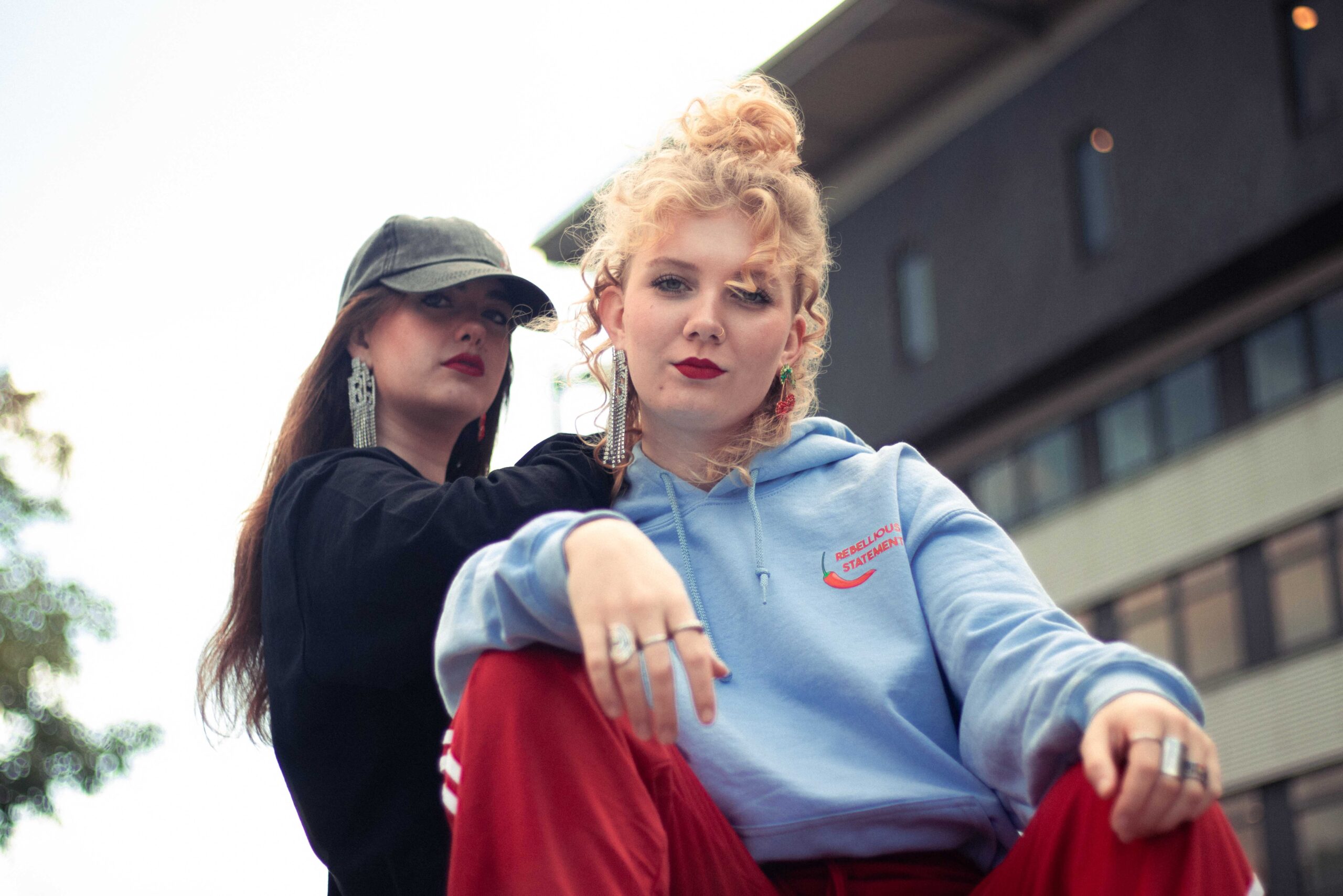 Twee vrouwen met een stoere pose kijken de camera in met een stadse achtergrond.